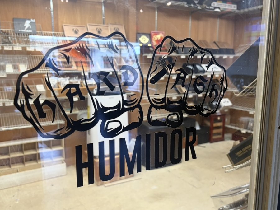 The Hard Ash Humidor entrance decal and cigar shelves at BBQ City Cigars